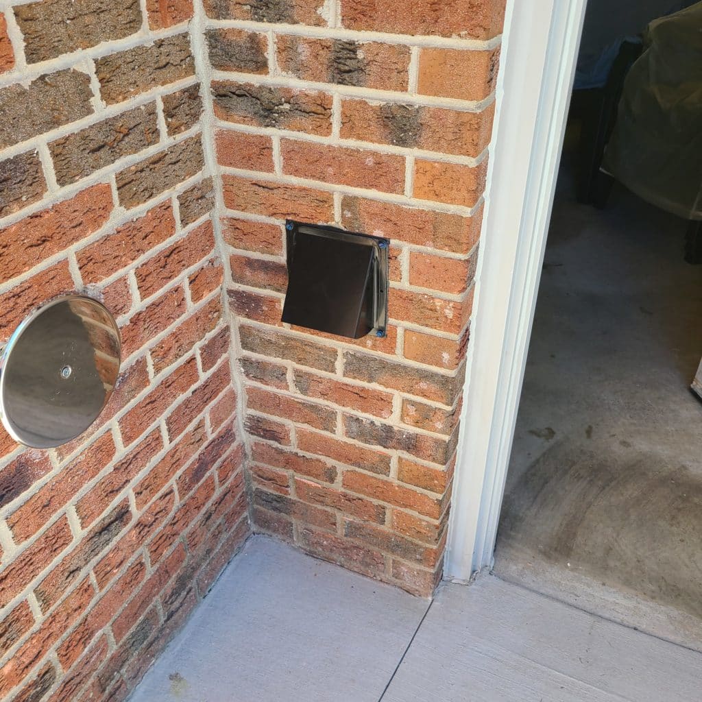 Black ground level dryer vent on brick exterior